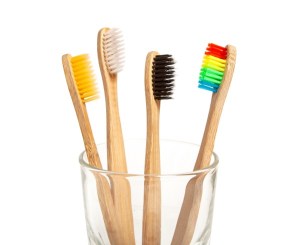 4 tooth brushes in a cup. 1 with yellow bristles, 1 with white bristles, 1 with black bristles, and 1 with rainbow bristles.