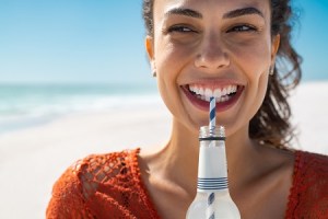 A woman smiling on the beach with a drink with a straw