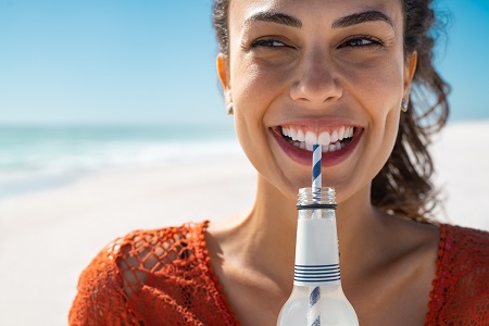 A woman smiling on the beach with a drink with a straw